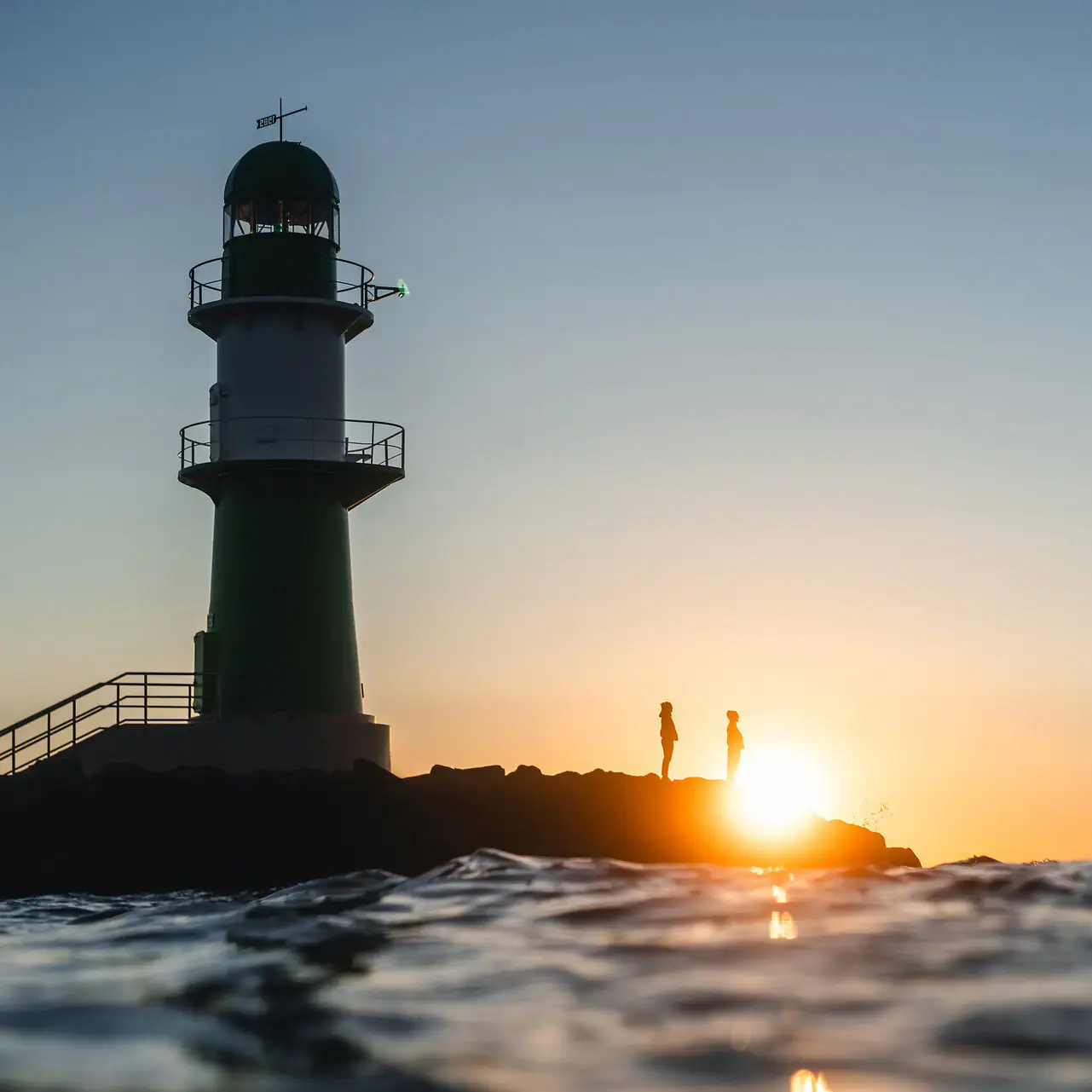 Angebote im aja Warnemünde Leuchtturm im Wasser bei Sonnenuntergang