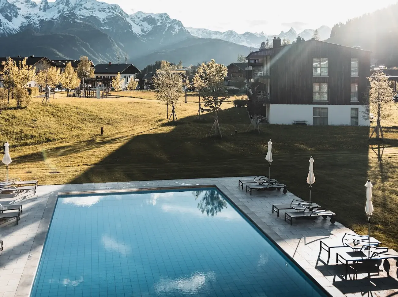 Swimmingpool mit Stühlen und Sonnenschirmen vor dem Bergresort Werfenweng mit Bergen im Hintergrund.