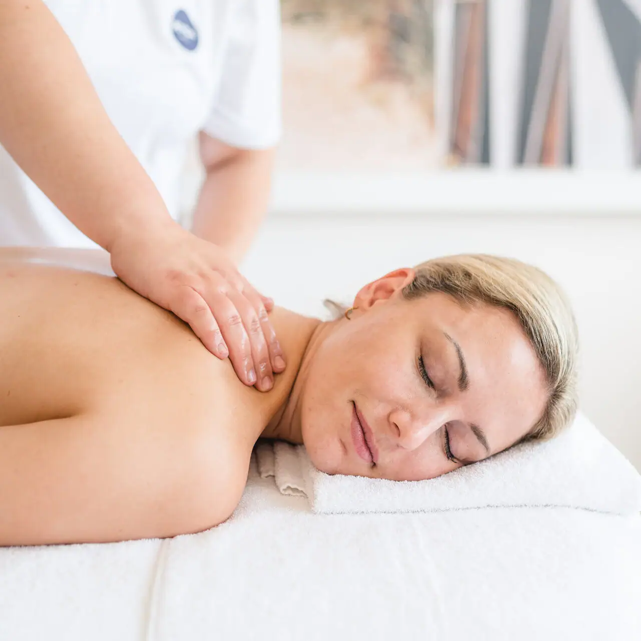 Massage Eine Frau liegt mit geschlossenen Augen auf einem weißen Handtuch.