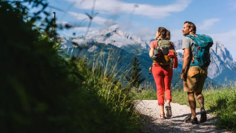 Wanderungen Garmisch Ein Mann und eine Frau wandern auf einem Pfad mit Bergen im Hintergrund.