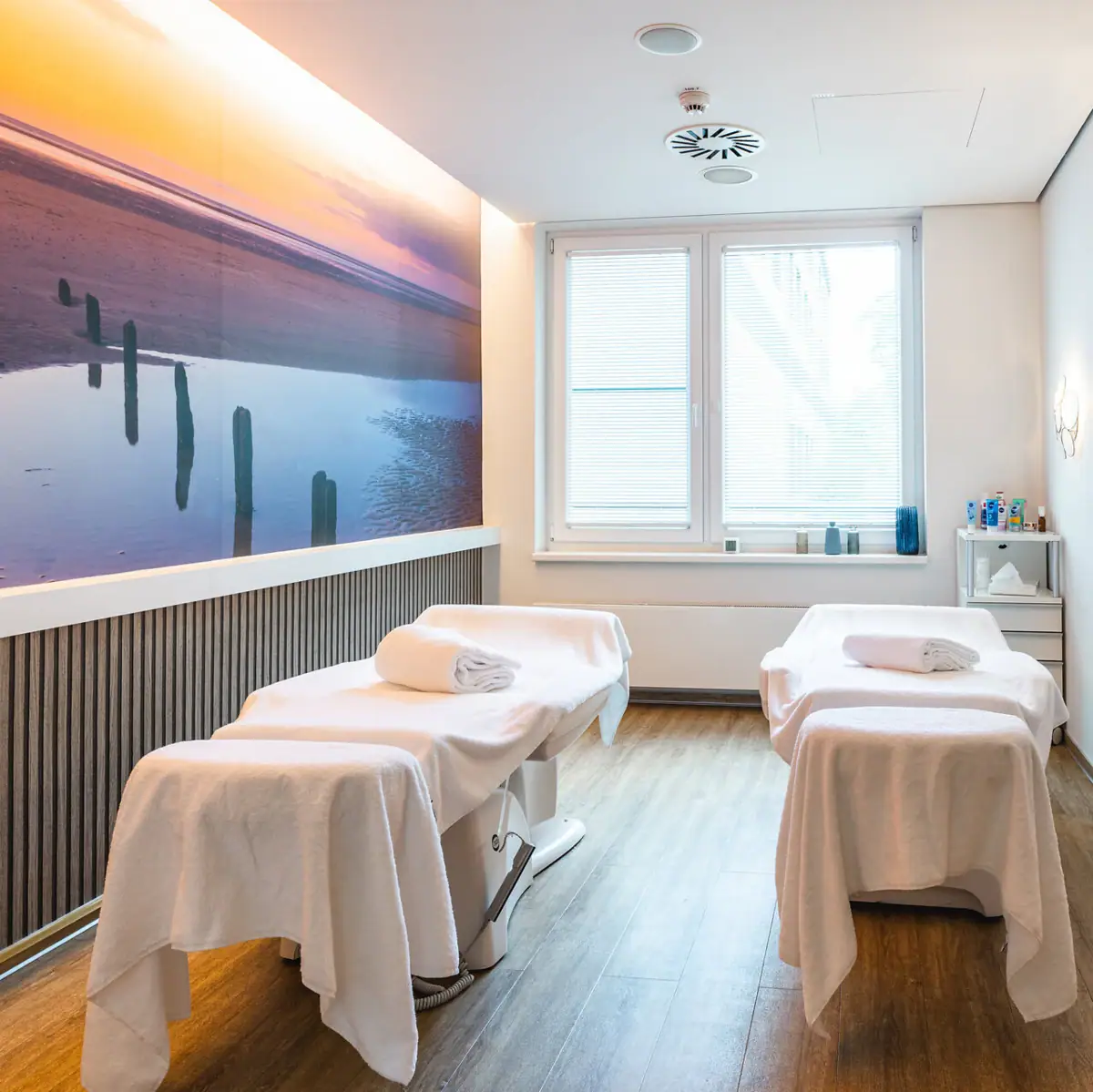 Massage Ein Raum mit Liegen und einem Gemälde an der Wand.