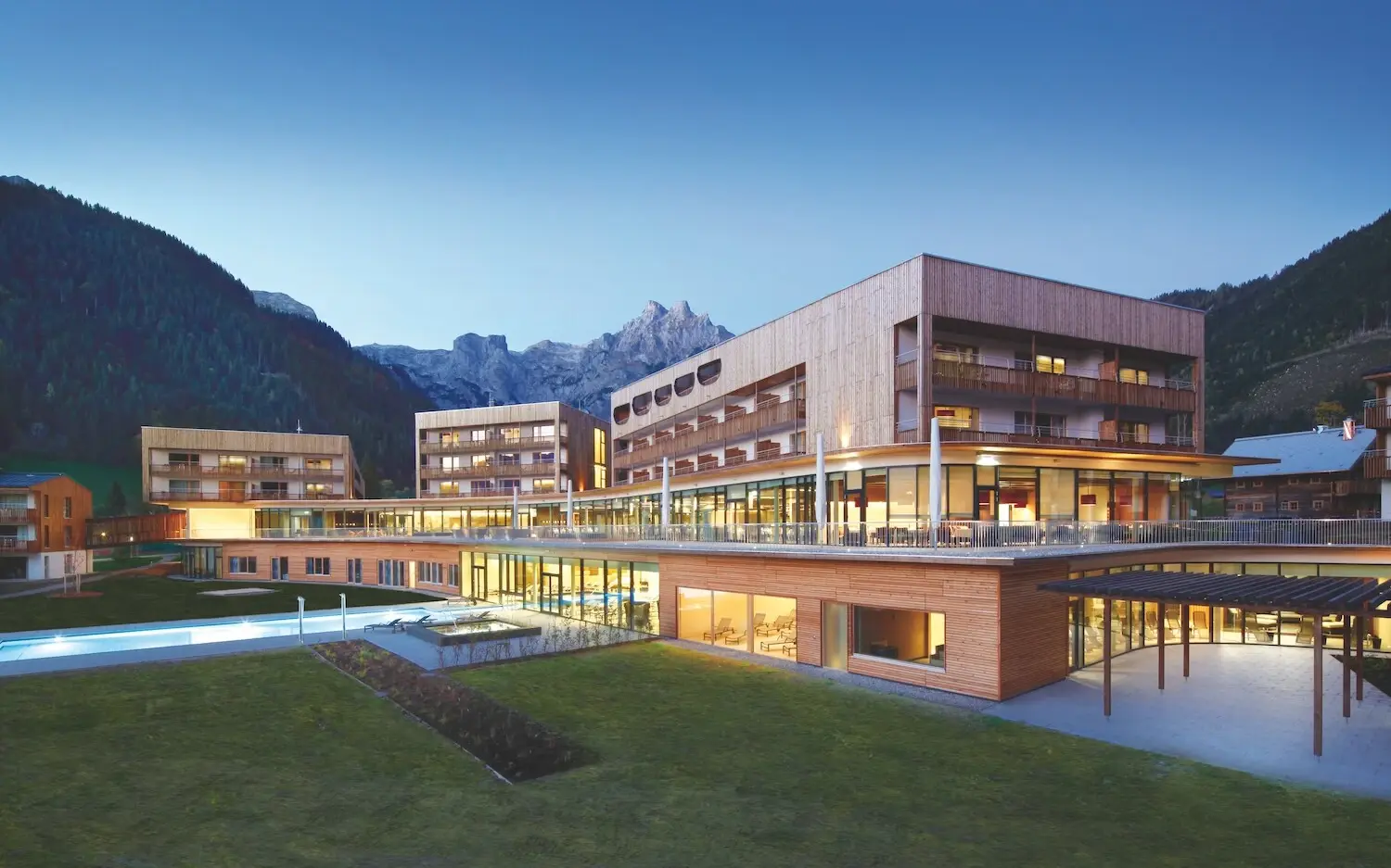 The aja Werfenweng with lawn and swimming pool surrounded by trees and mountains.