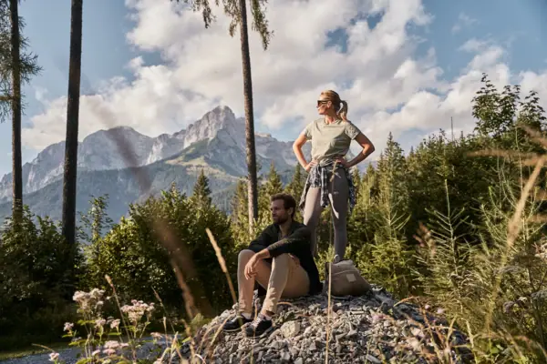Ein Mann und eine Frau stehen auf einem Felsen vor einem Berg.