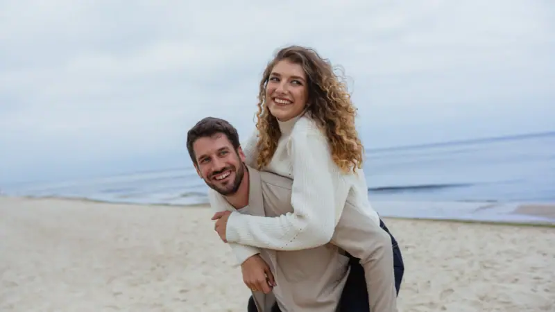 Ein Mann trägt eine Frau auf dem Rücken am Strand.