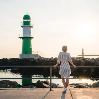 Eine Frau steht auf einem Steg neben einem grün-weißen Leuchtturm.