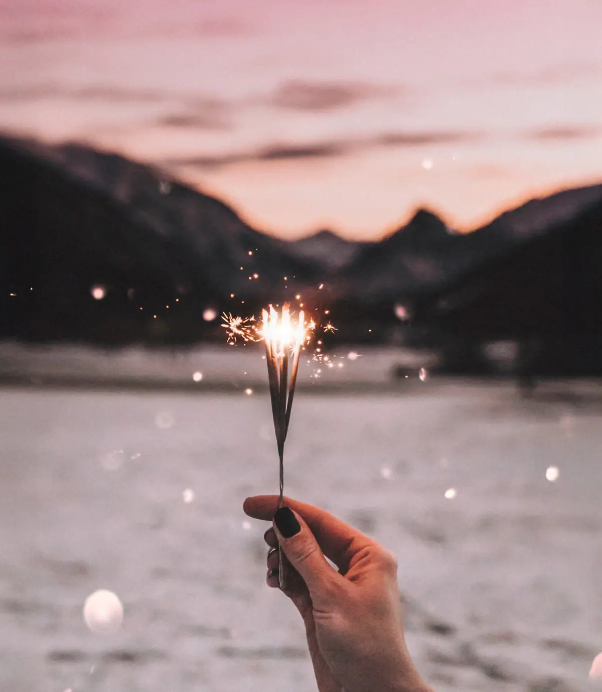 Hand hält eine Wunderkerze vor einem Himmel im Hintergrund die Berge