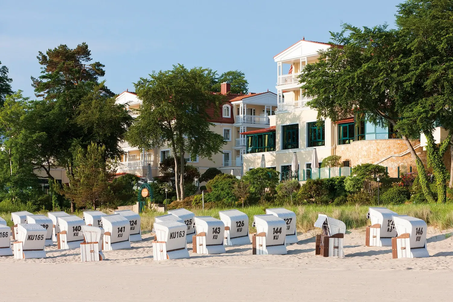 There are many white beach chairs on a beach and the aja Bansin can be seen in the background.