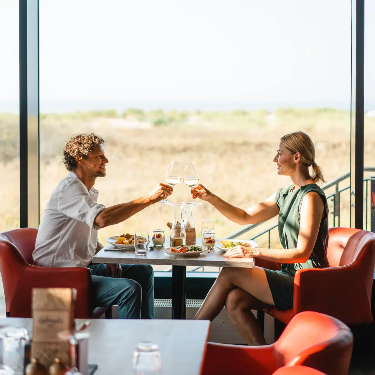 Restaurant im aja Warnemünde Ein Mann und eine Frau sitzen an einem Tisch mit Speisen und Getränken.