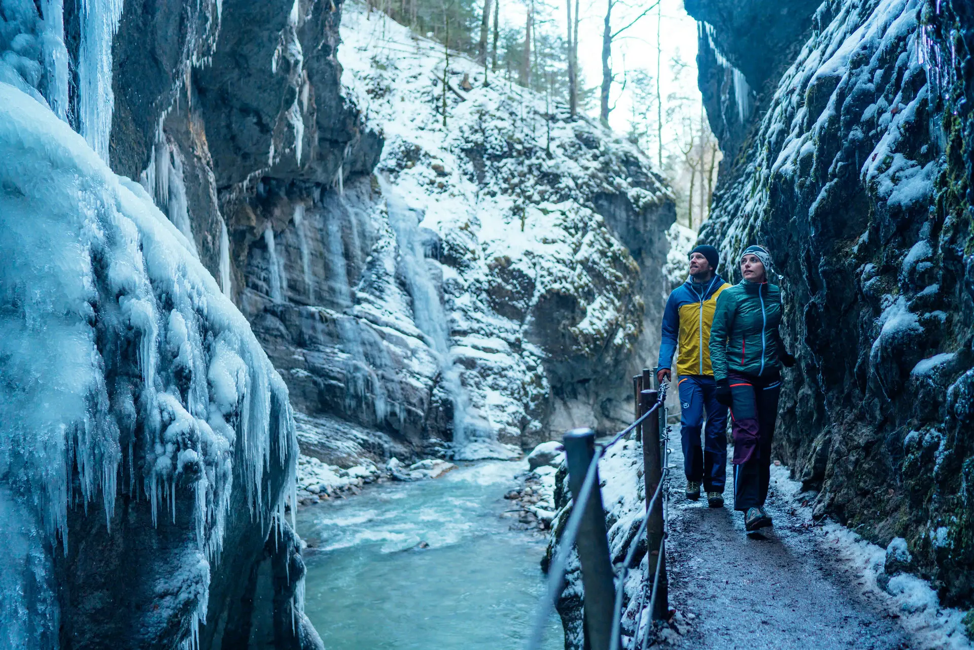 Ein Mann und eine Frau gehen auf einem Weg in einer verschneiten Schlucht.