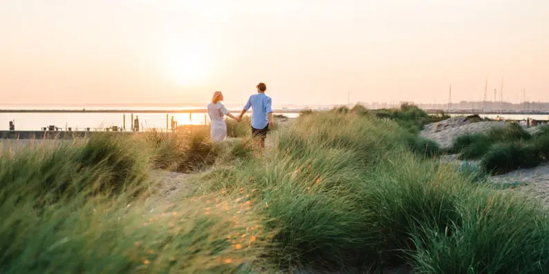 Mann und Frau halten Hände in einer grasbewachsenen Landschaft.