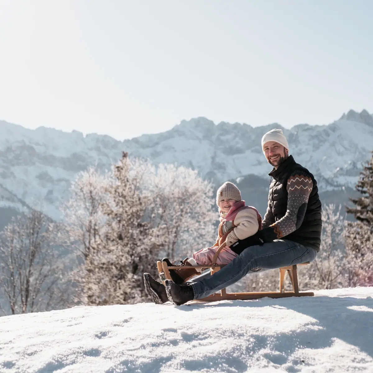 Ein Vater mit seiner Tochter auf einem Schlitten beim Familienurlaub in Garmisch-Partenkirchen.