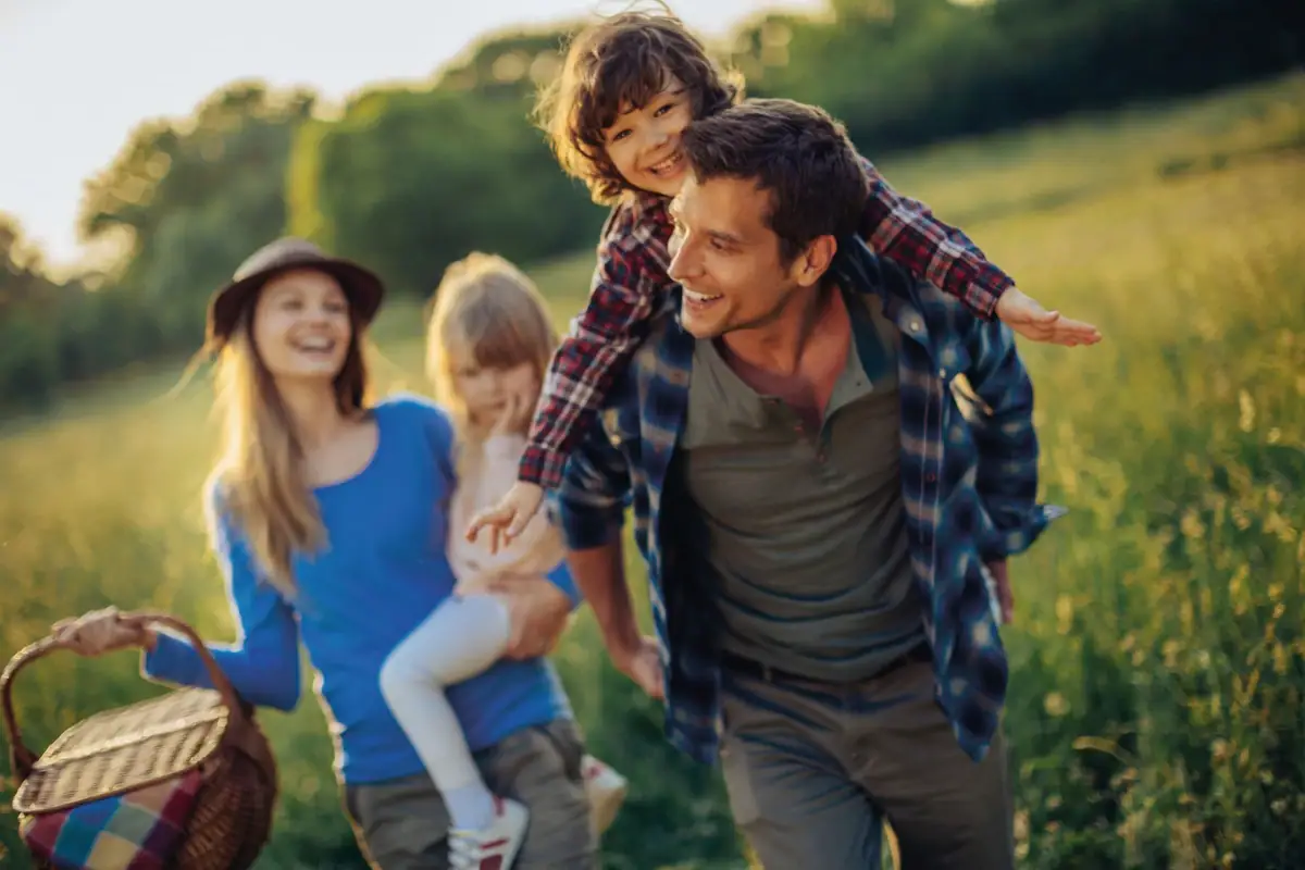 Ein Mann trägt ein Kind auf seinen Schultern im Freien bei einem Familienausflug.