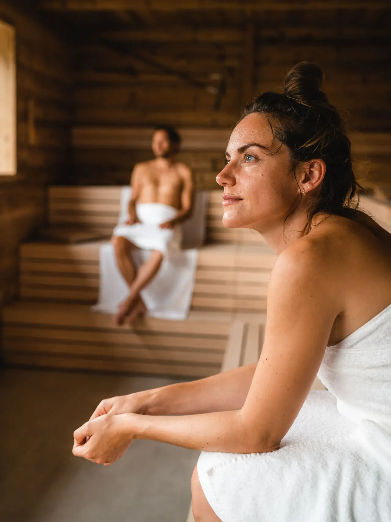 Frau und ein Mann sitzen mit weißen Handtüchern in einer Sauna.