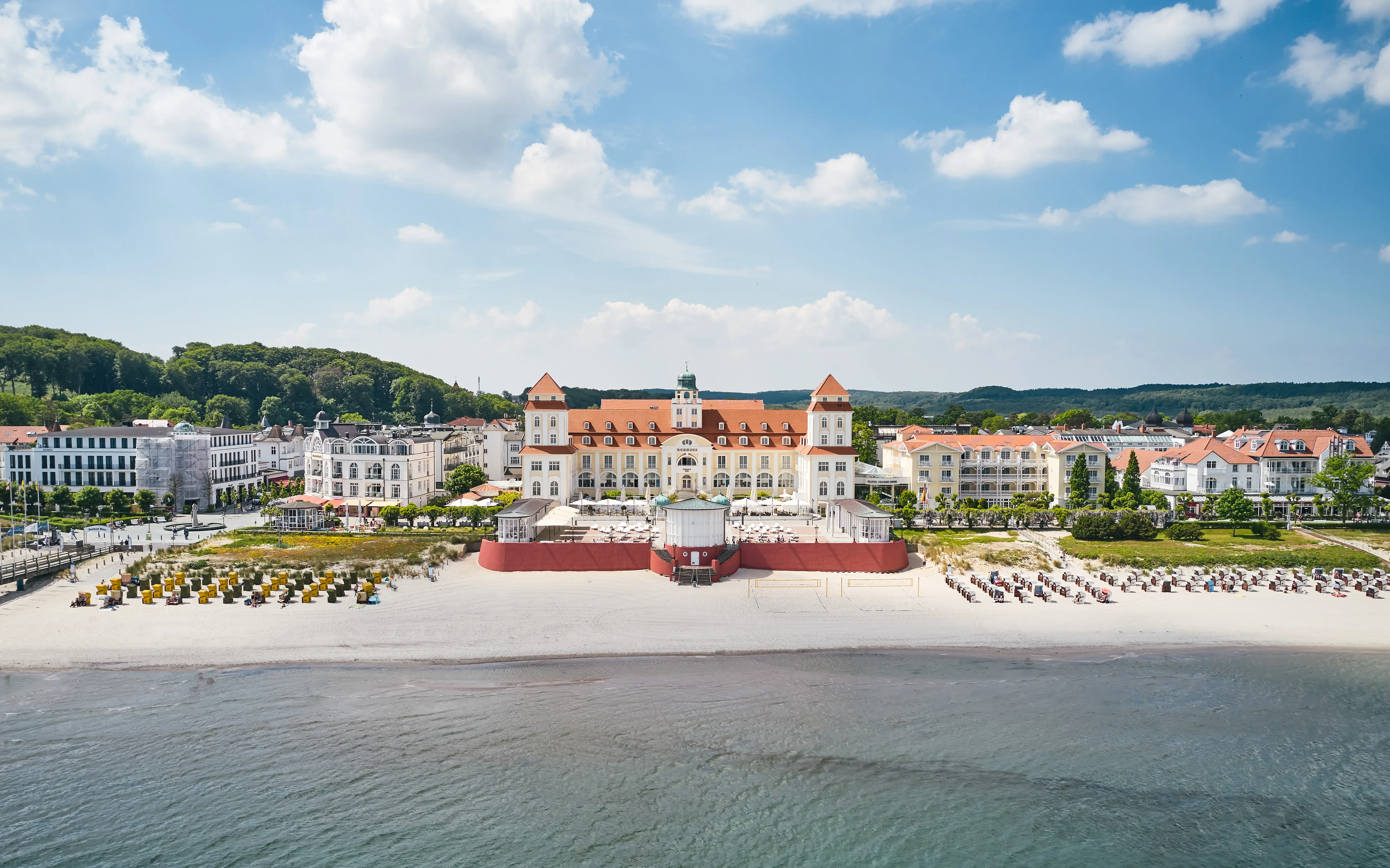 Großes weißes Gebäude mit roten Dächern an einem Strand neben einem Gewässer.