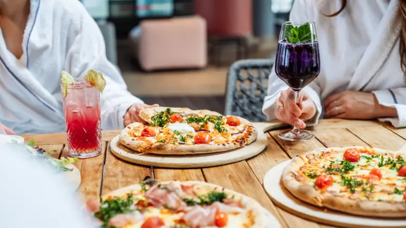 Eine Gruppe von Menschen sitzt an einem Tisch mit Pizzen und Getränken.