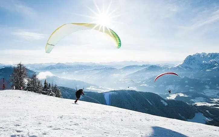 Gruppe von Personen beim Paragliden auf einem verschneiten Berg.