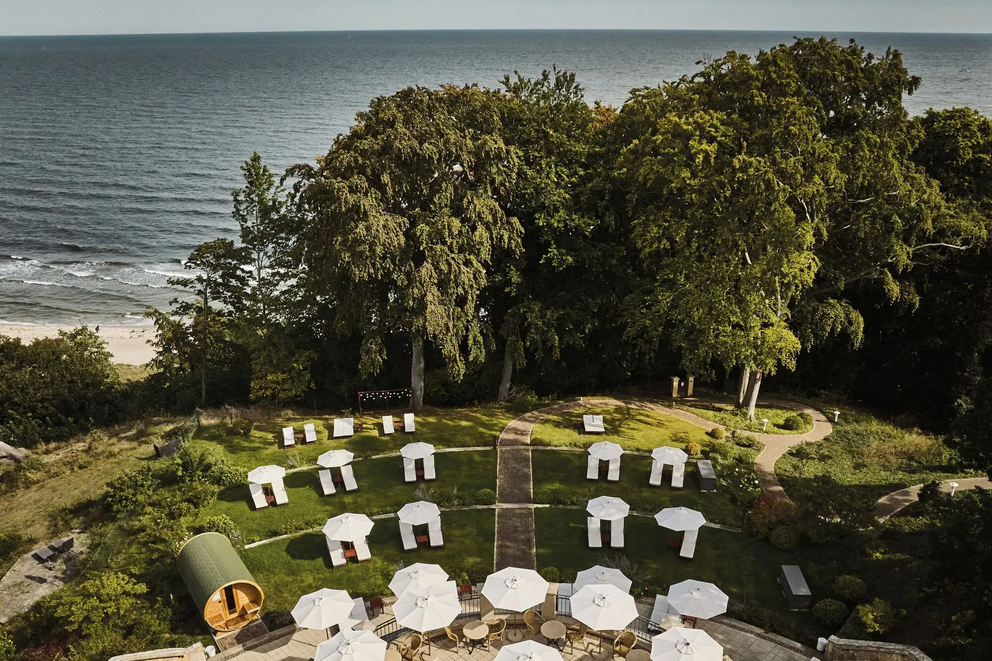 Liegewiese Eine Gruppe von weißen Liegestühlen und Sonnenschirmen auf einer grasbewachsenen Fläche mit Bäumen und Wasser.