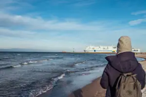 Ostsee Warnemünde Eine Person betrachtet ein Schiff am Strand.