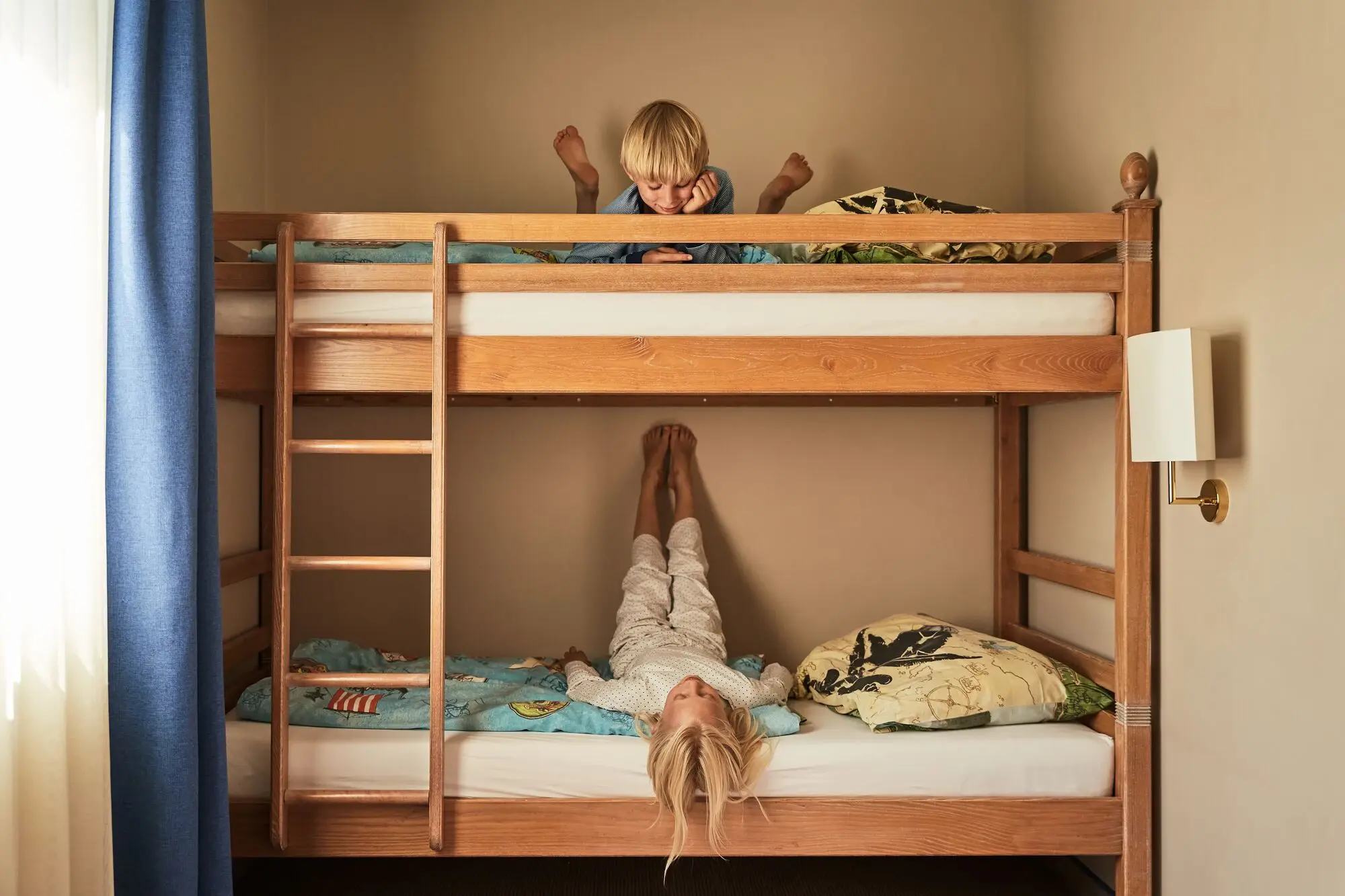 One child lies at the bottom and one at the top of a bunk bed with a ladder.