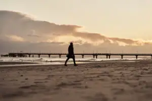 Eine Person geht am Strand entlang bei Sonnenuntergang.