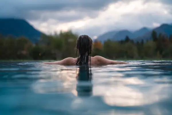 Eine Frau schwimmt im Pool des aja Ruhpolding mit Blick auf die Berge.