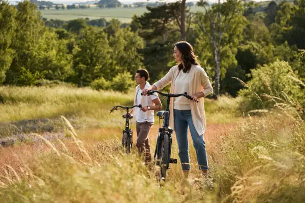 Paar mit Fahrrädern steht inmitten einer sommerlichen Wiesenlandschaft auf Rügen; sie genießen den Ausblick über die hügelige Natur und blühende Felder unter freiem Himmel.
