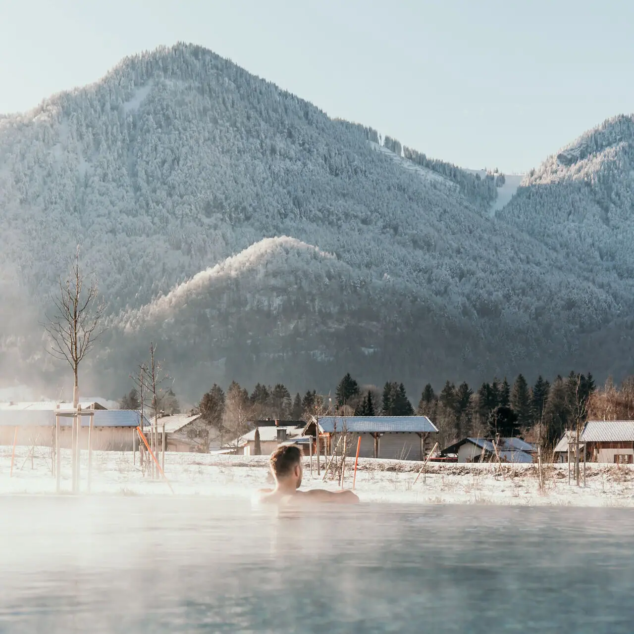 Außenpool im Winter Eine Person in einem Pool mit Bergen im Hintergrund.