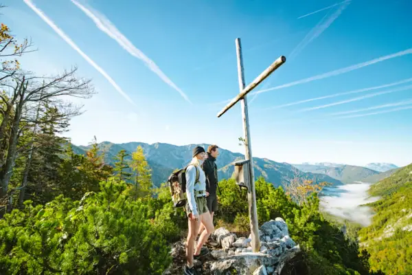 Zwei Personen stehen auf einem Felsen mit einem Kreuz auf einem Berg.