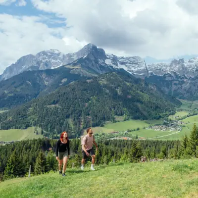 Ein Mann und eine Frau wandern auf einem Hügel mit Bergen im Hintergrund.