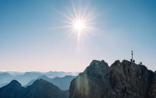 Sonne scheint über der Zugspitze mit Gipfelkreuz.