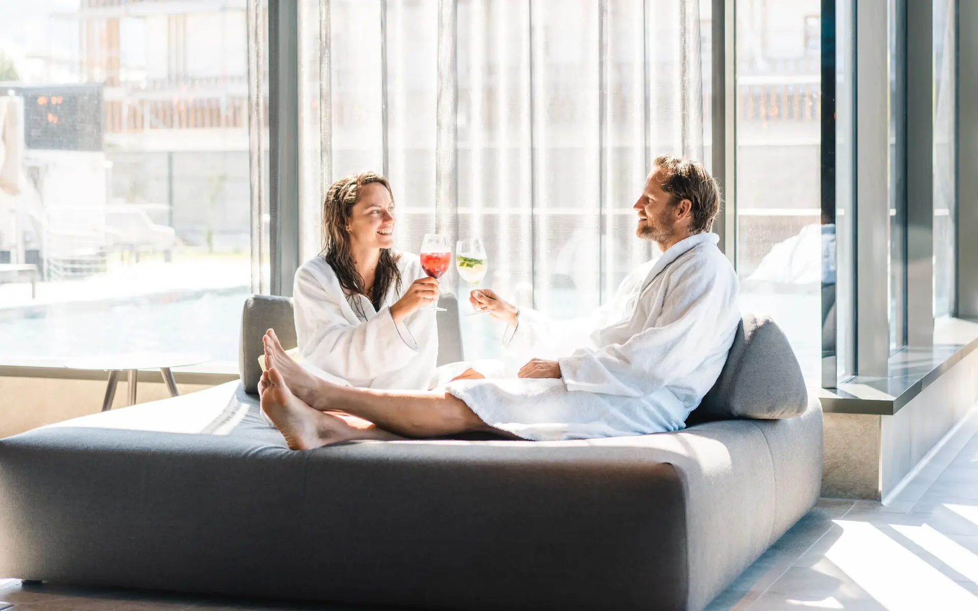 Ein Mann und eine Frau stoßen an und entspannen in Bademänteln im Loungebereich des SPA aja Garmisch-Partenkirchen 