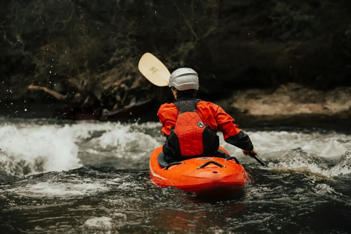 Eine Person in einem Kajak mit Schwimmweste und Paddel auf einem Fluss.