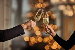 Sektgläser Hände halten Sektgläser und im Hintergrund sind Lichterketten zu erkennen.