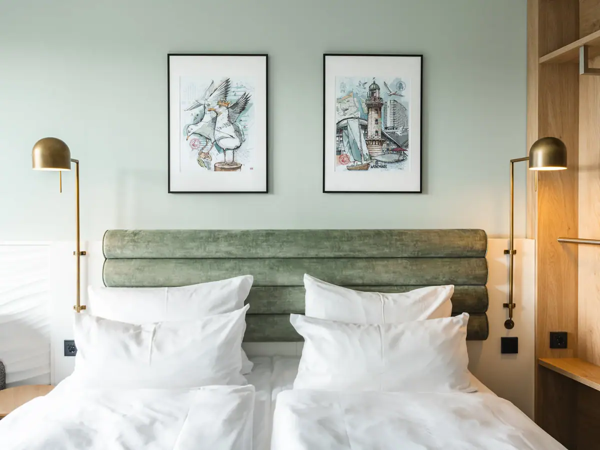 Zimmer aja Warnemünde Ein Bett mit weißen Kissen und einem grünen Kopfteil, flankiert von zwei Lampen.