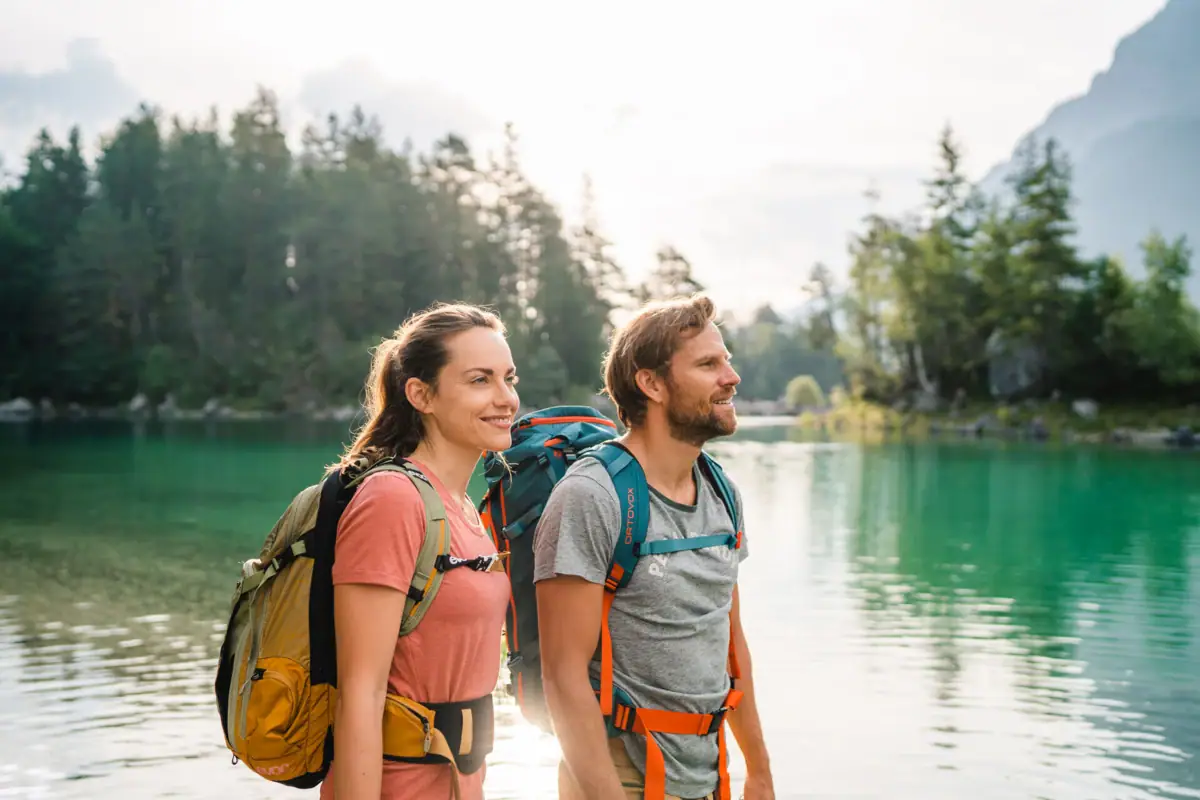 Eibsee Wanderung Ein Mann und eine Frau mit Rucksäcken stehen vor einem Gewässer.
