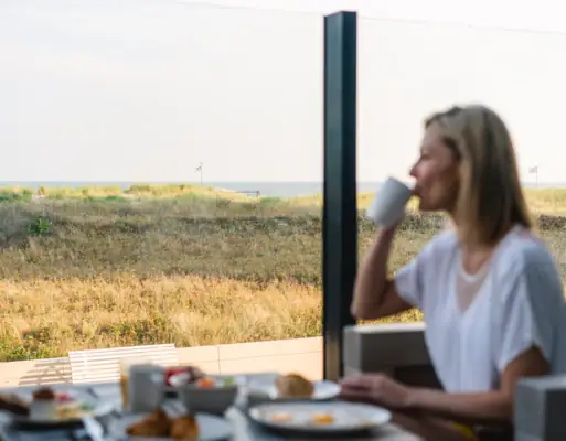 Frühstück im aja Warnemünde Eine Frau sitzt an einem Tisch mit einer Tasse Kaffee.