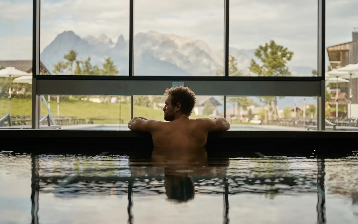 Mann schwimmt in einem Pool mit Berg- und Baumblick.