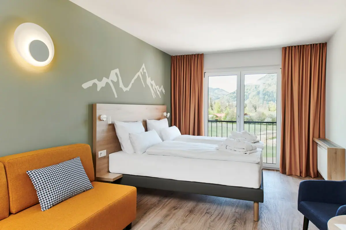 Zimmer mit französischem Balkon im aja Ruhpolding Ein Raum mit zwei Betten und einem Sofa.