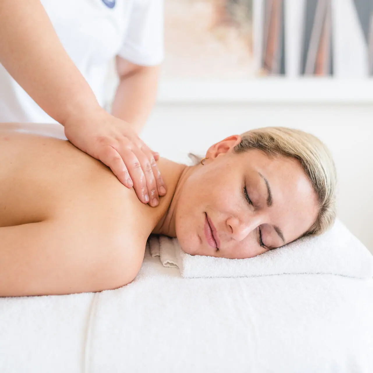 Anwendungen im aja Warnemünde Eine Frau liegt mit geschlossenen Augen auf einem weißen Handtuch.