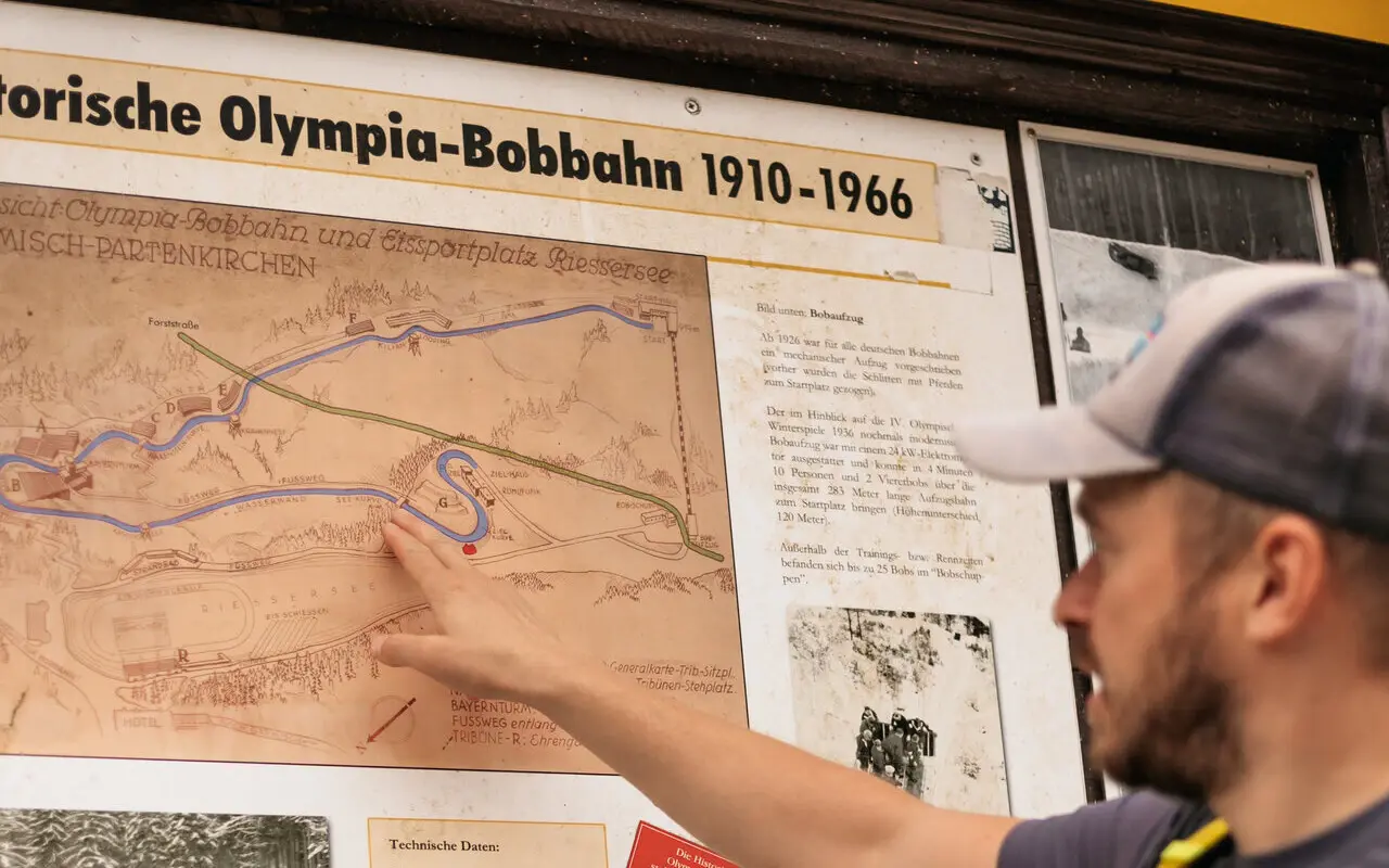 Ein Mann verfolgt die historischen Bobbahn Ruten auf einem Schild nach. 