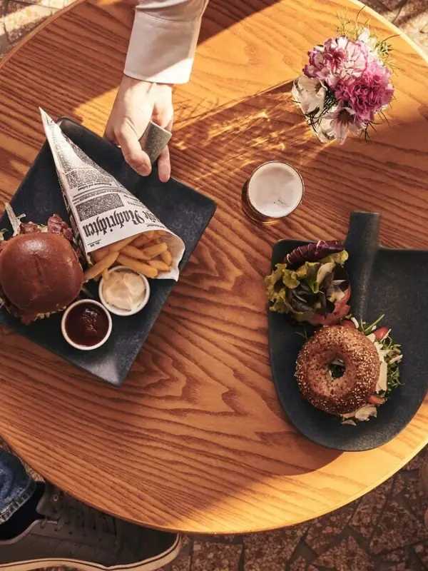 Eine Person hält einen Teller mit Essen an einem Tisch.