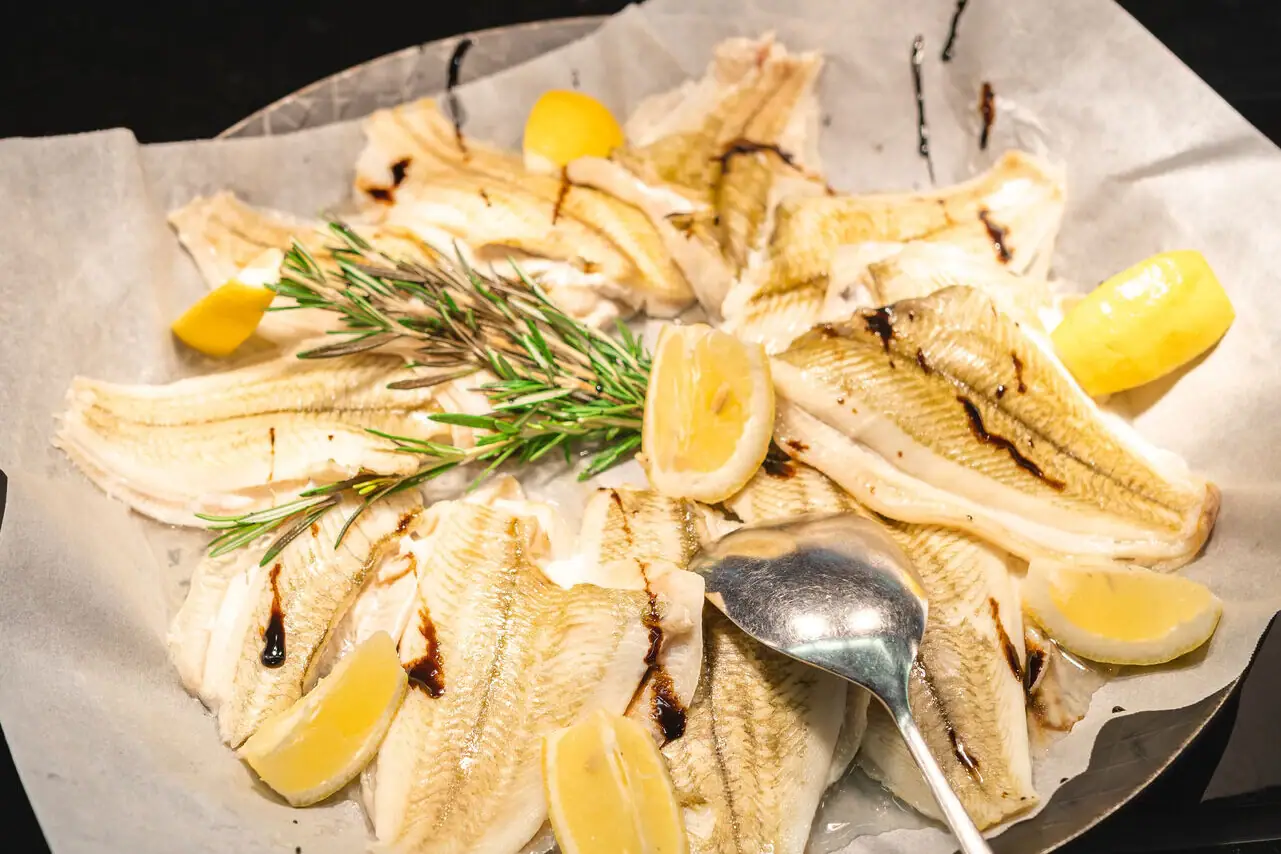 Ein Teller mit Fisch und Zitronenscheiben, daneben ein Löffel.