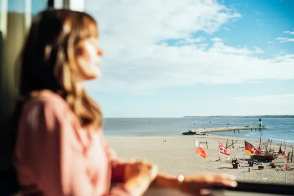 Eine Frau schaut aus einem Fenster auf einen Strand.