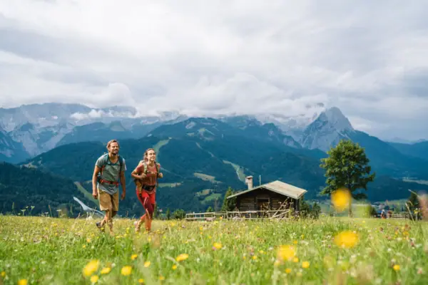 Ein Mann und eine Frau wandern im Sommer in Garmisch-Partenkirchen in den Bergen im Hintergrund.