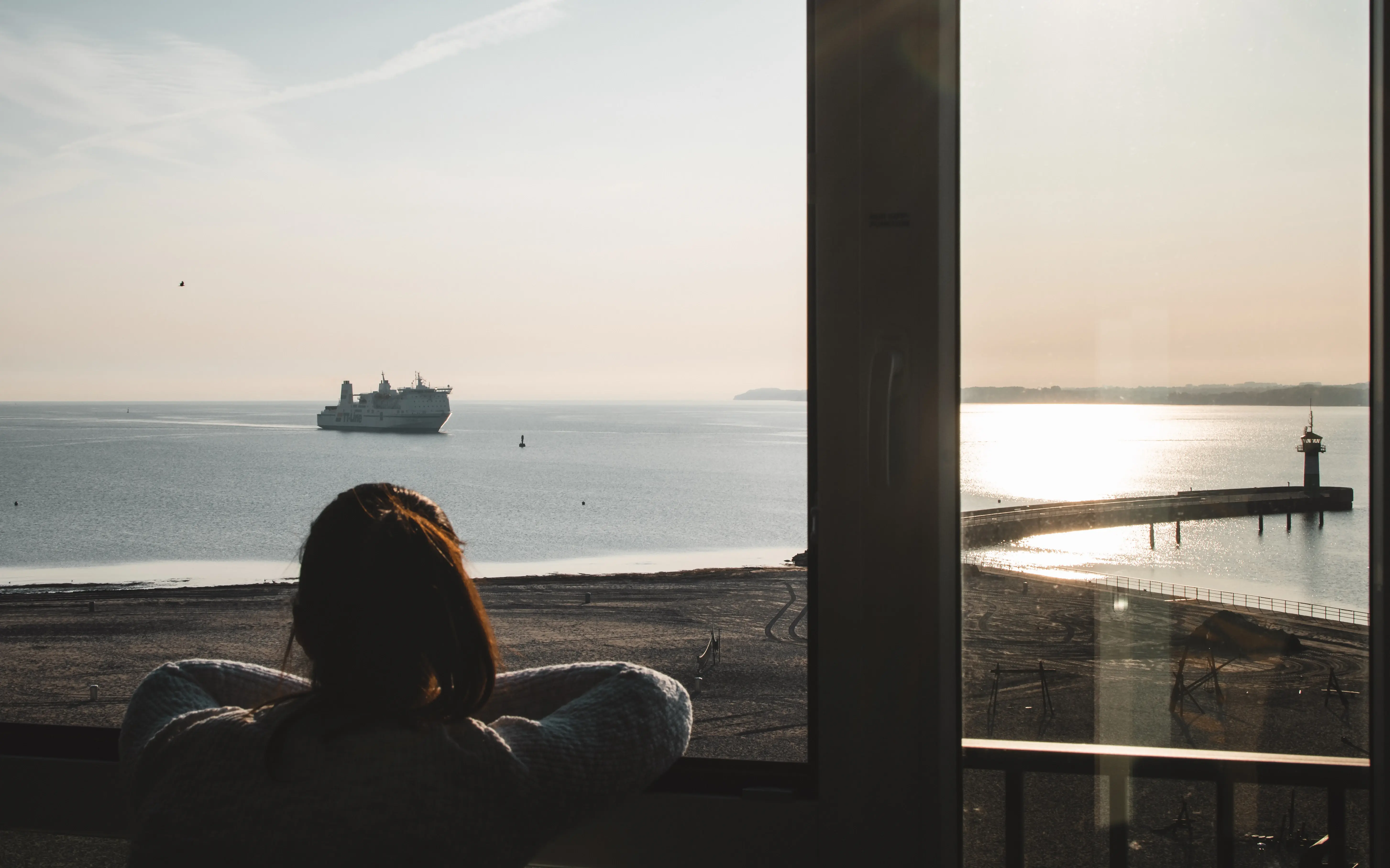Frau blickt aus dem Fenster auf ein Schiff im Wasser