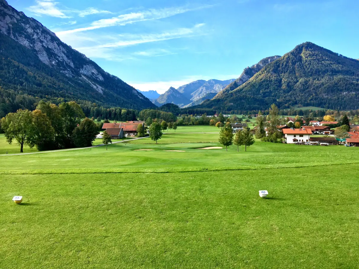 Ein Golfplatz in Ruhpolding mit Bäumen und Bergen im Hintergrund.