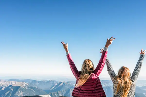 Aussicht Zugspitze Zwei Frauen mit erhobenen Armen, die in den Himmel schauen.
