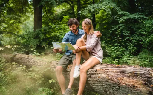Ein Mann und eine Frau sitzen auf einem Baumstamm und betrachten eine Karte.