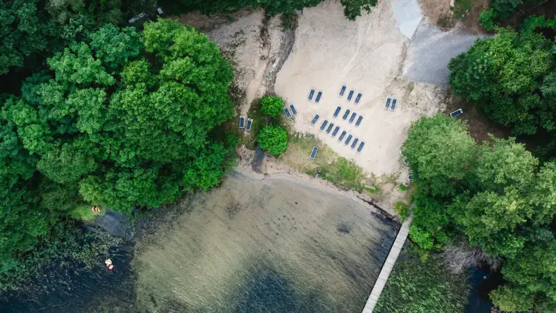 aja Bad Saarow Ein Steg über einem Gewässer mit Stühlen und Bäumen.