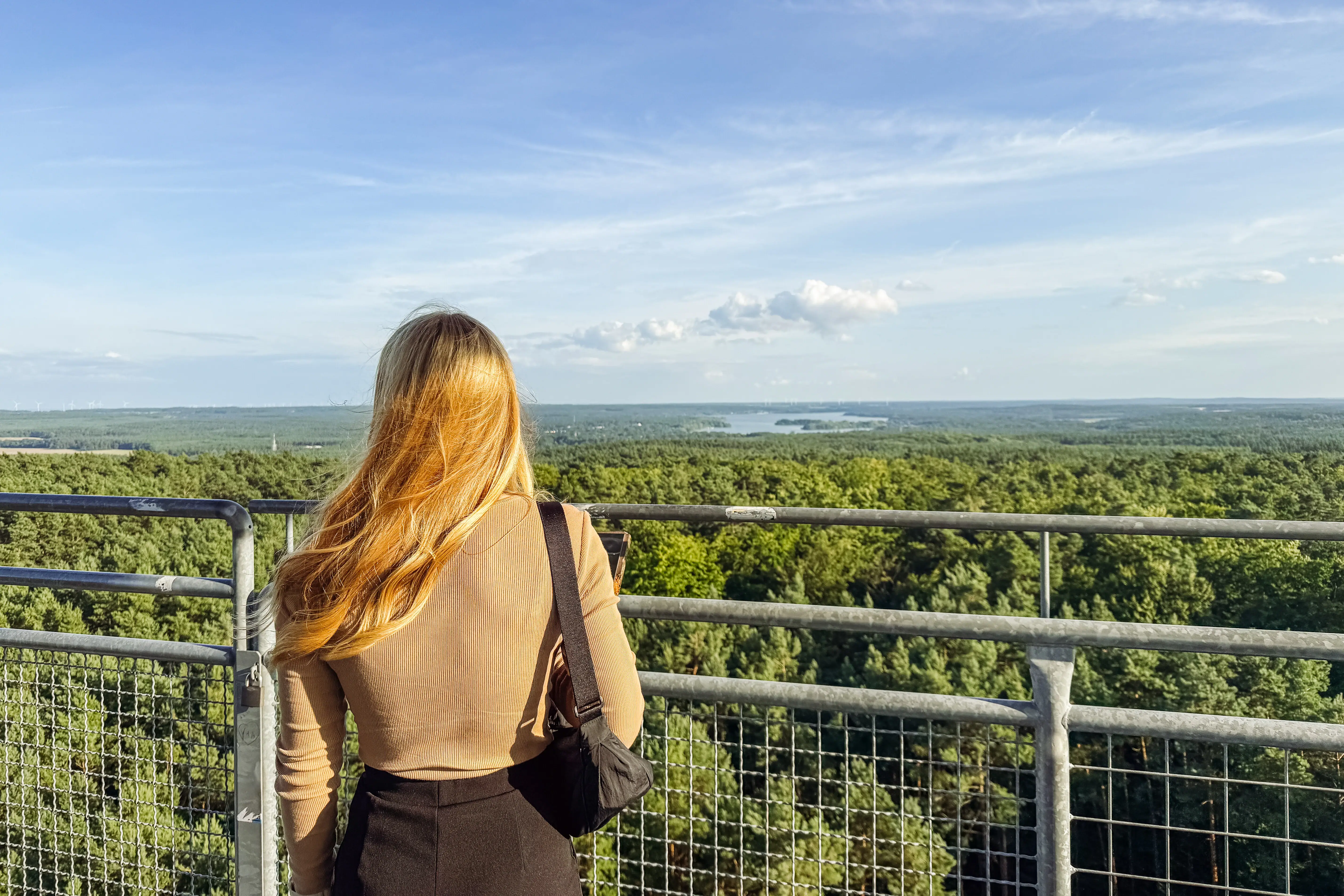 Eine Frau steht auf einem Balkon mit Blick auf einen Wald.